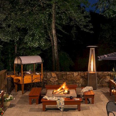 Outdoor patio with a fire pit, seating, and forest in the background at night.