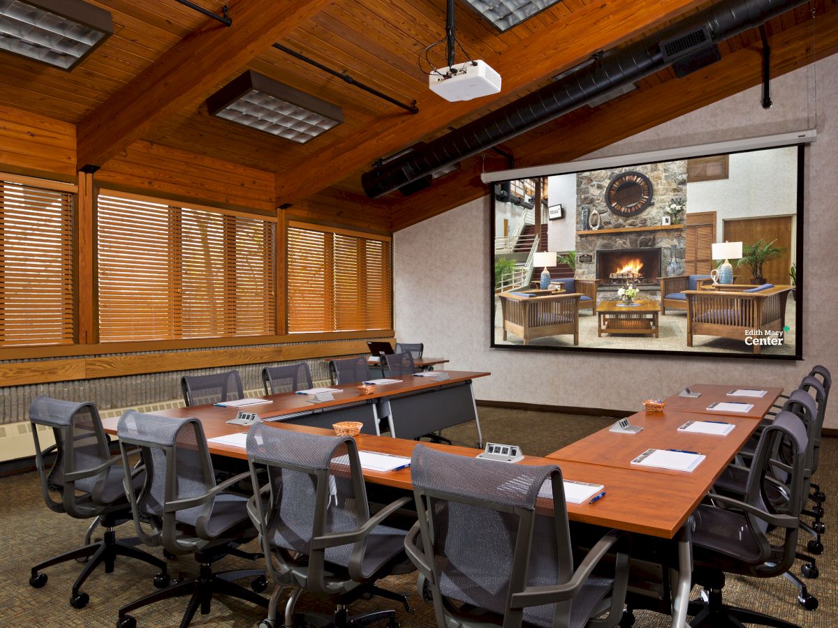 Conference room with a long table, chairs, and a fireplace image on the screen.