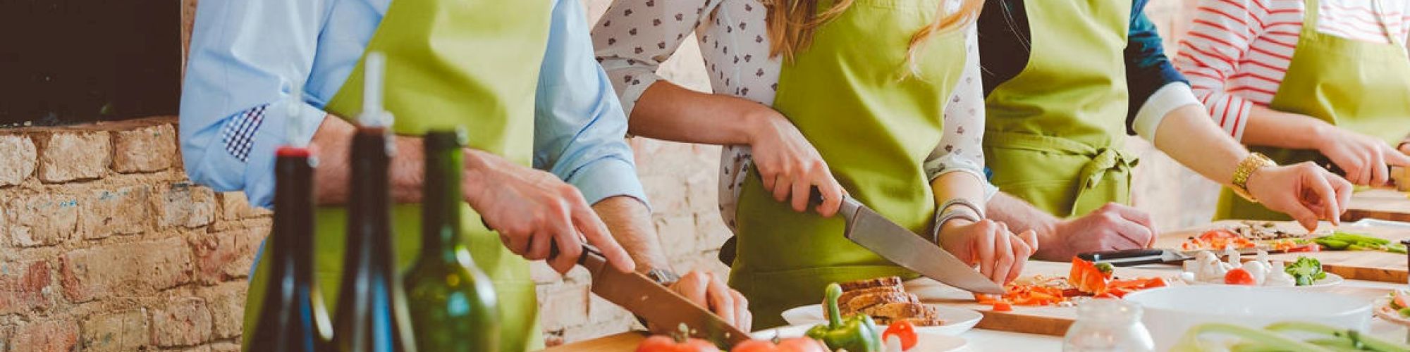 People in aprons are cooking together, chopping vegetables on a table.