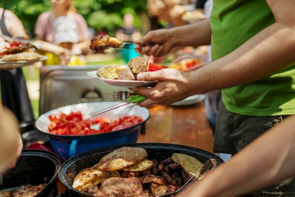 A person serves food from a buffet of grilled meats and fresh salad outdoors.