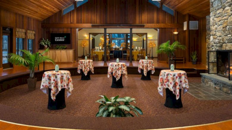 An elegant lobby with wooden walls, a stone fireplace, tables with cloths, and a welcome desk.