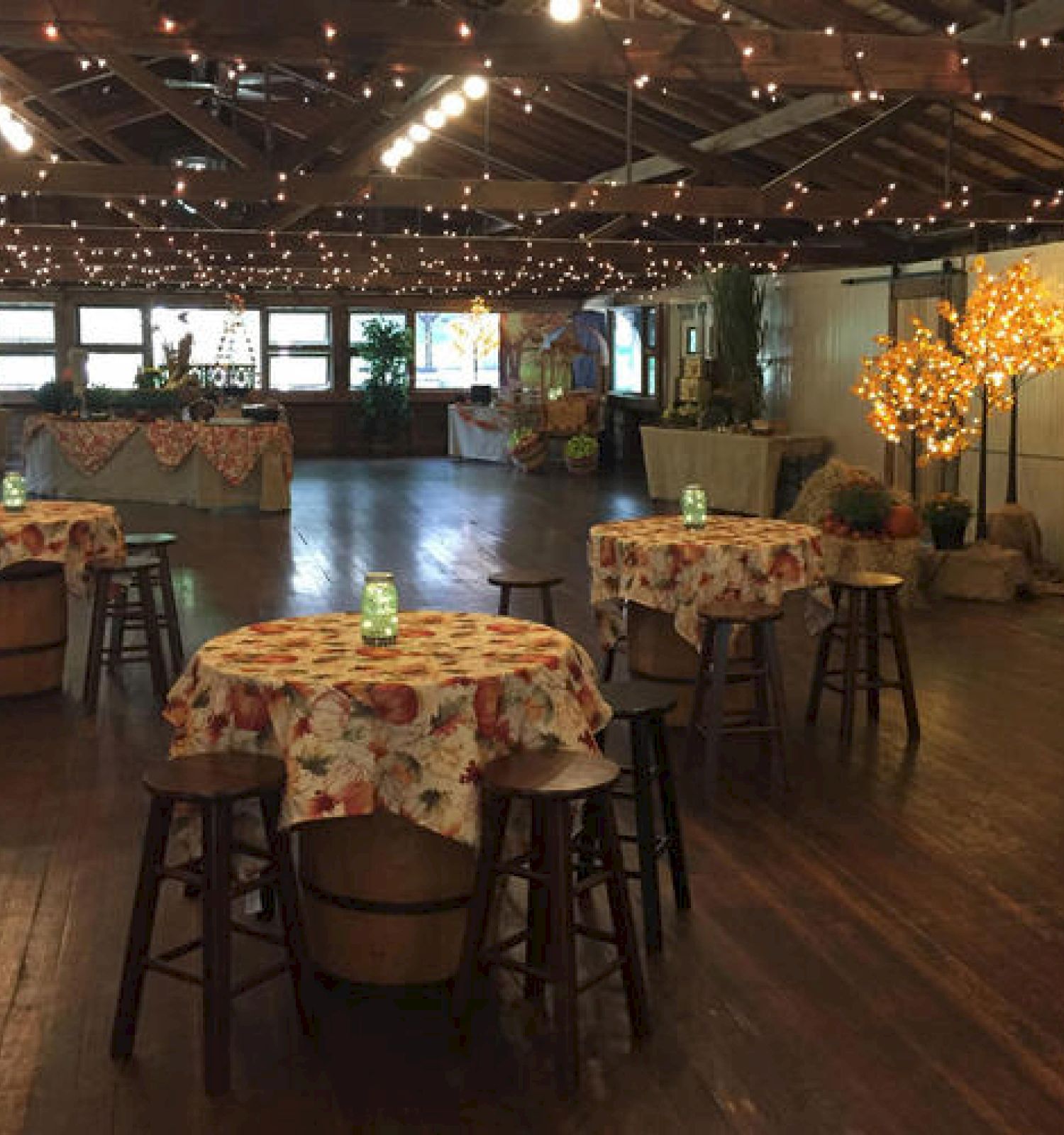 Cozy indoor event space with tables, festive decor, string lights, and a fireplace.