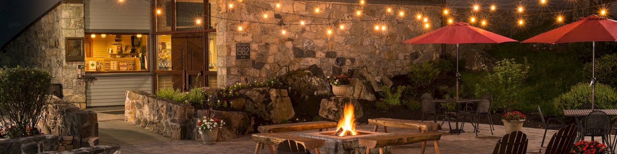 Cozy backyard patio at dusk with fire pit, string lights, chairs, and a house with interior lights on.