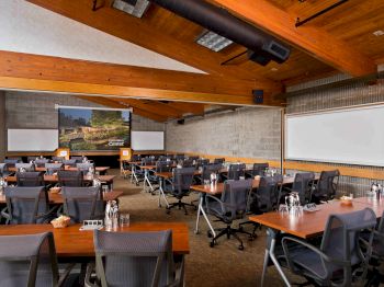 A conference room with tables, chairs, and presentation screens awaits attendees.