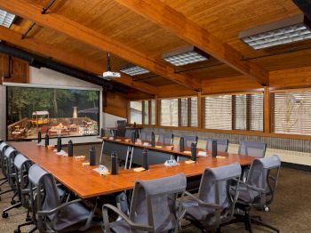 A conference room with a long table, chairs, artwork, and wood-paneled ceiling.