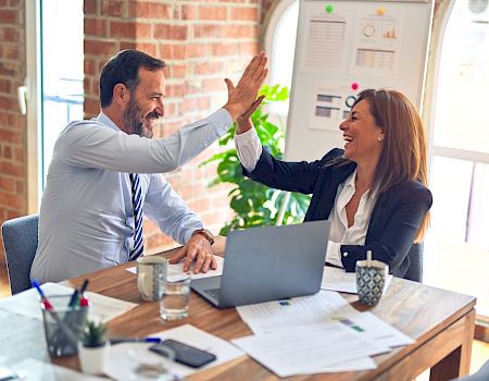 Two professionals are high-fiving in an office setting, likely celebrating a success.