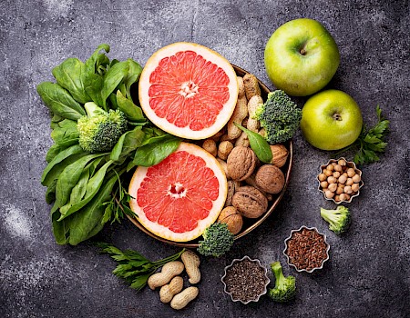 A variety of healthy foods including fruits, nuts, greens, and seeds on a dark background.