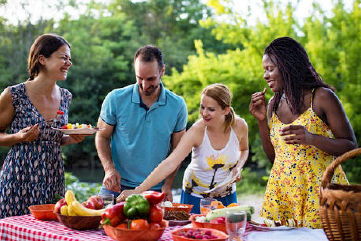 Four people enjoying a picnic with fresh fruit and food on a sunny day.