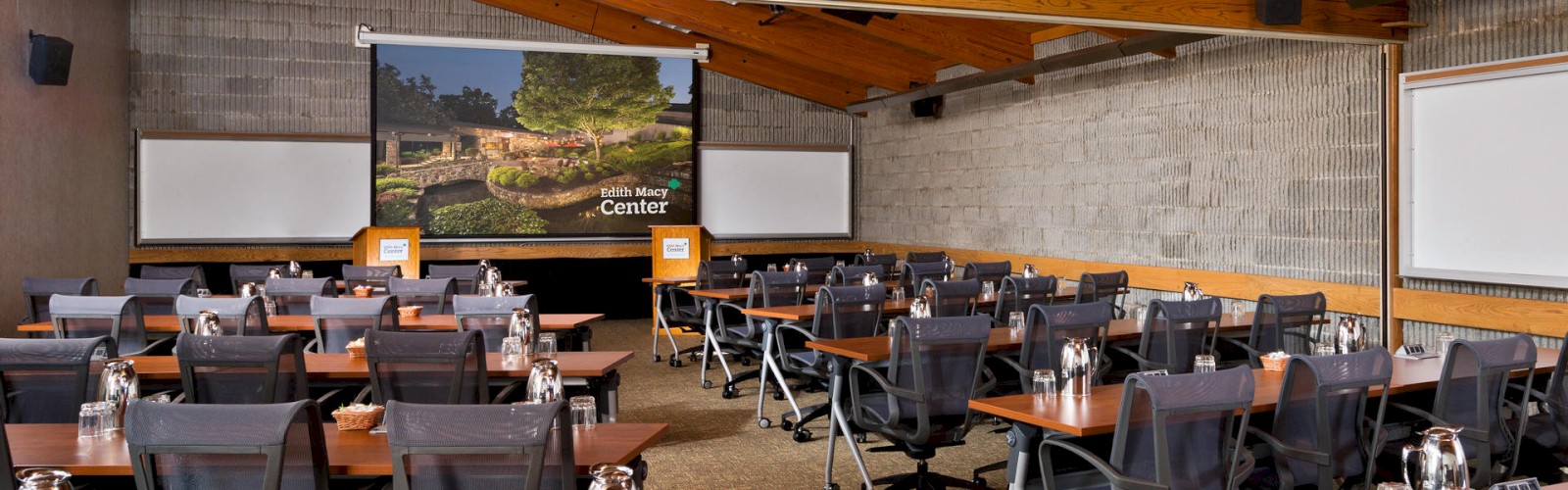 A conference room with chairs, tables, water bottles, and presentation screens.