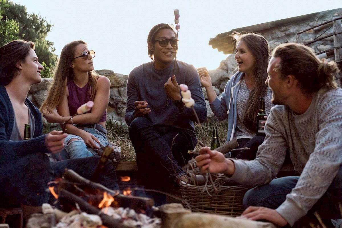 A group of friends is roasting marshmallows over a fire, enjoying each other's company outdoors.