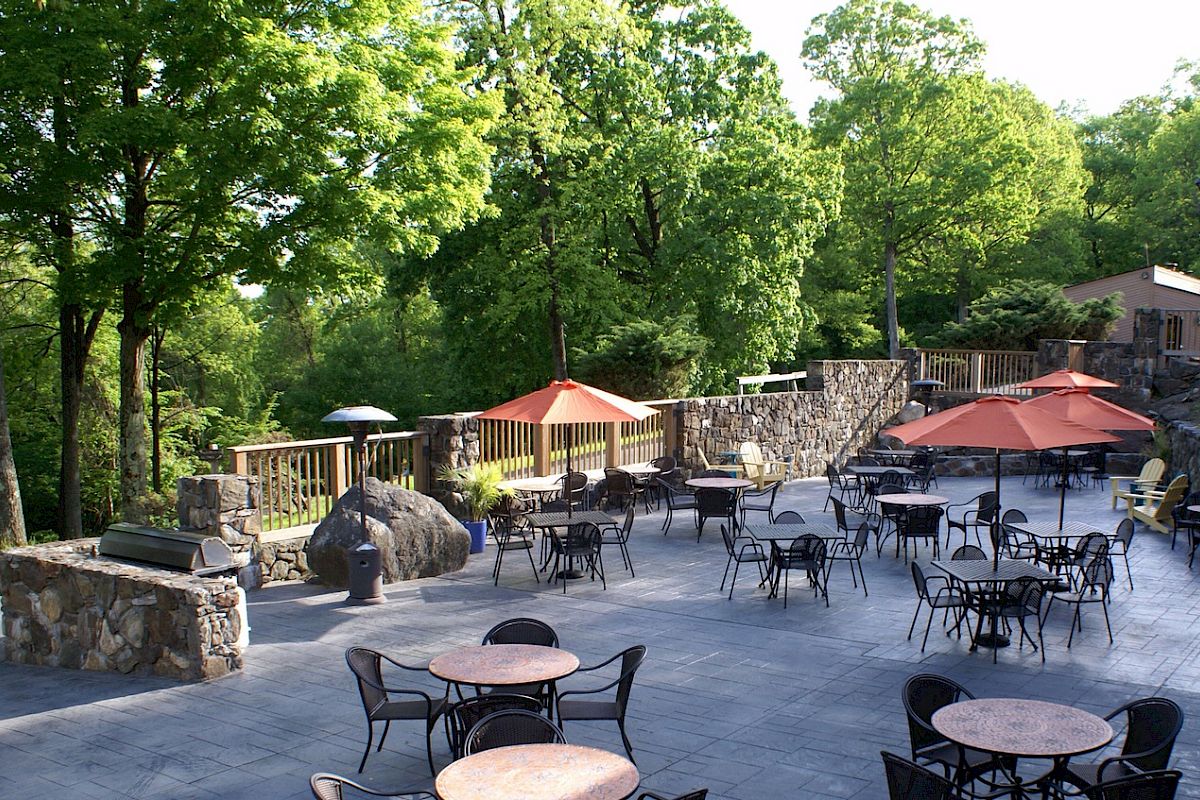 Outdoor patio with tables, chairs, umbrellas, surrounded by trees.