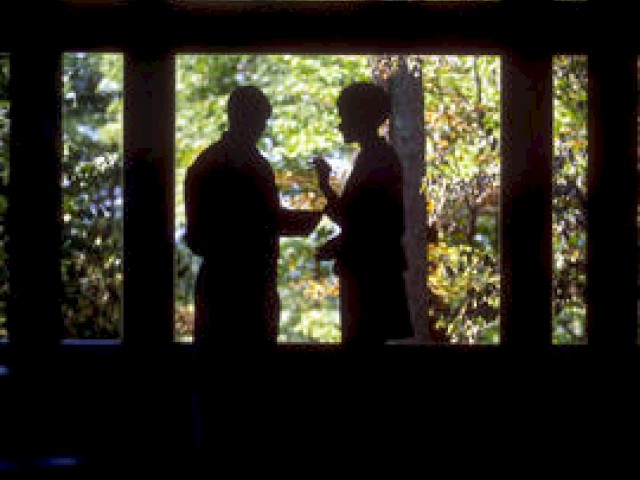Two silhouetted figures stand by a window, possibly conversing.
