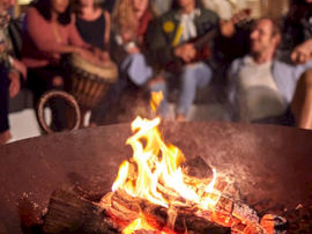 People gather around a campfire, possibly enjoying an outdoor event.
