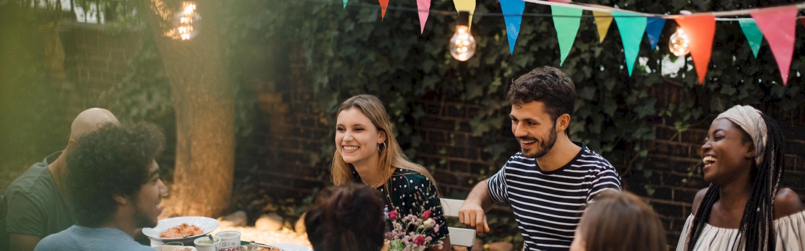 People dining outdoors under string lights and festive flags.