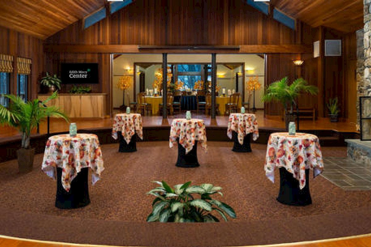 An elegant lobby with wooden walls, a stone fireplace, tables with cloths, and a welcome desk.