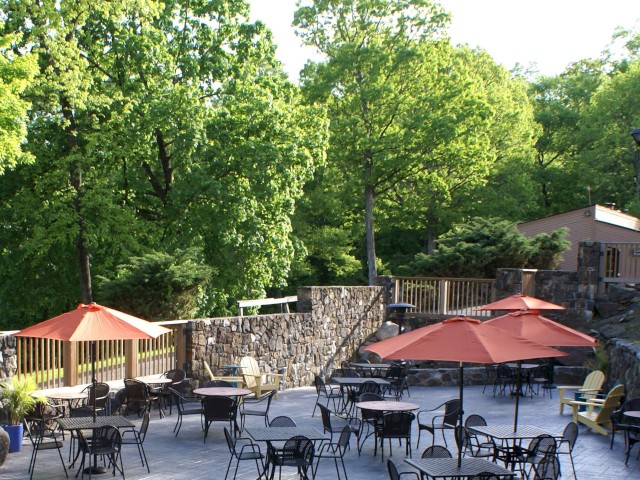 Outdoor patio with tables, chairs, and red umbrellas surrounded by trees.