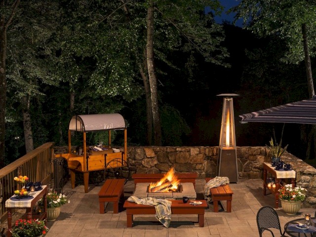A cozy outdoor patio with a fire pit, seating, and ambient lighting at night.