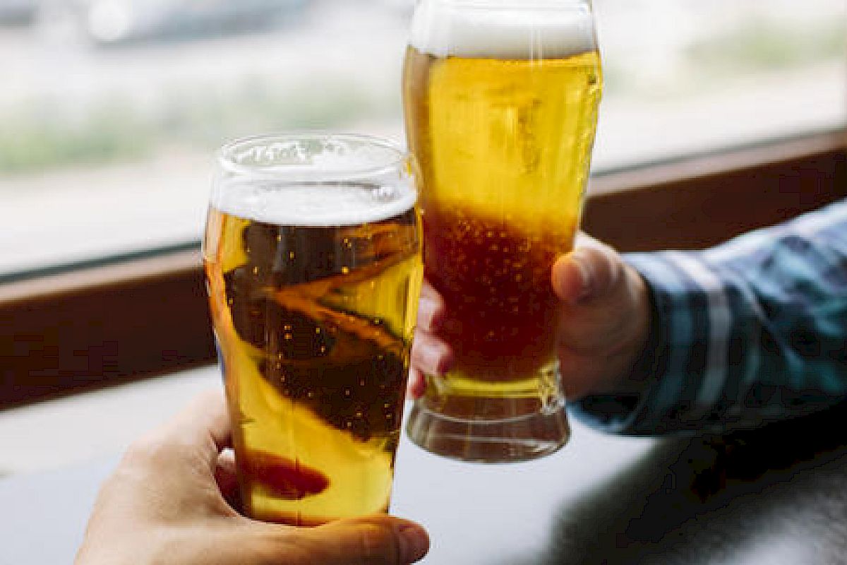 Two people are holding glasses of beer, seemingly making a toast inside a casual setting.