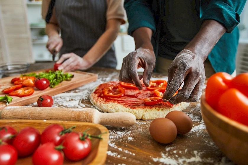 Two people preparing a pizza with fresh tomatoes and other ingredients.