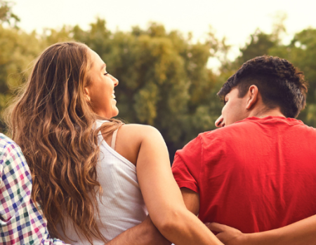 Group of friends sitting together outdoors with their arms around each other, facing away from the camera.