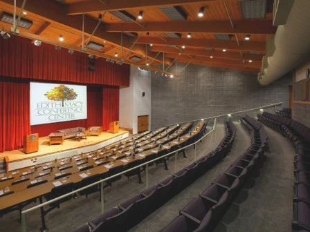 This image shows an auditorium with rows of empty seating, a stage with chairs, and a screen displaying "Edeh Umary Conference Center."