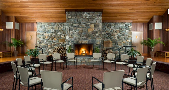 A cozy room with a stone fireplace surrounded by chairs and wooden walls, creating an inviting atmosphere.