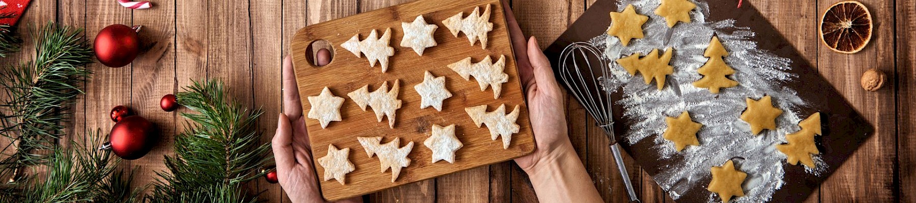 A festive scene with Christmas cookies being prepared on a wooden table, decorated with ornaments, dried oranges, and candy canes.