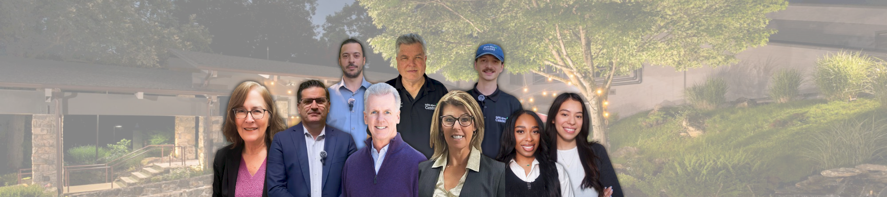The image shows a group of nine people standing in front of a scenic background with trees and a building.