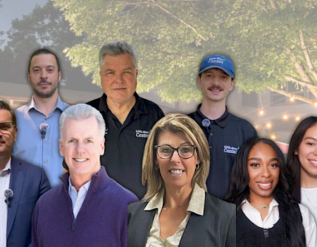 The image shows a group of nine people standing in front of a scenic background with trees and a building.