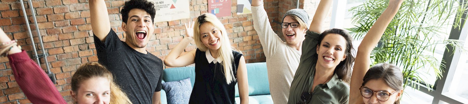 Group of cheerful people raising their arms in a lively office setting.