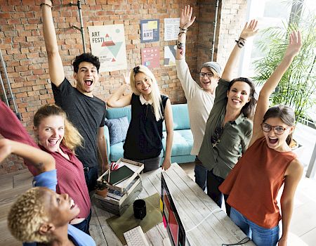 Group of cheerful people raising their arms in a lively office setting.